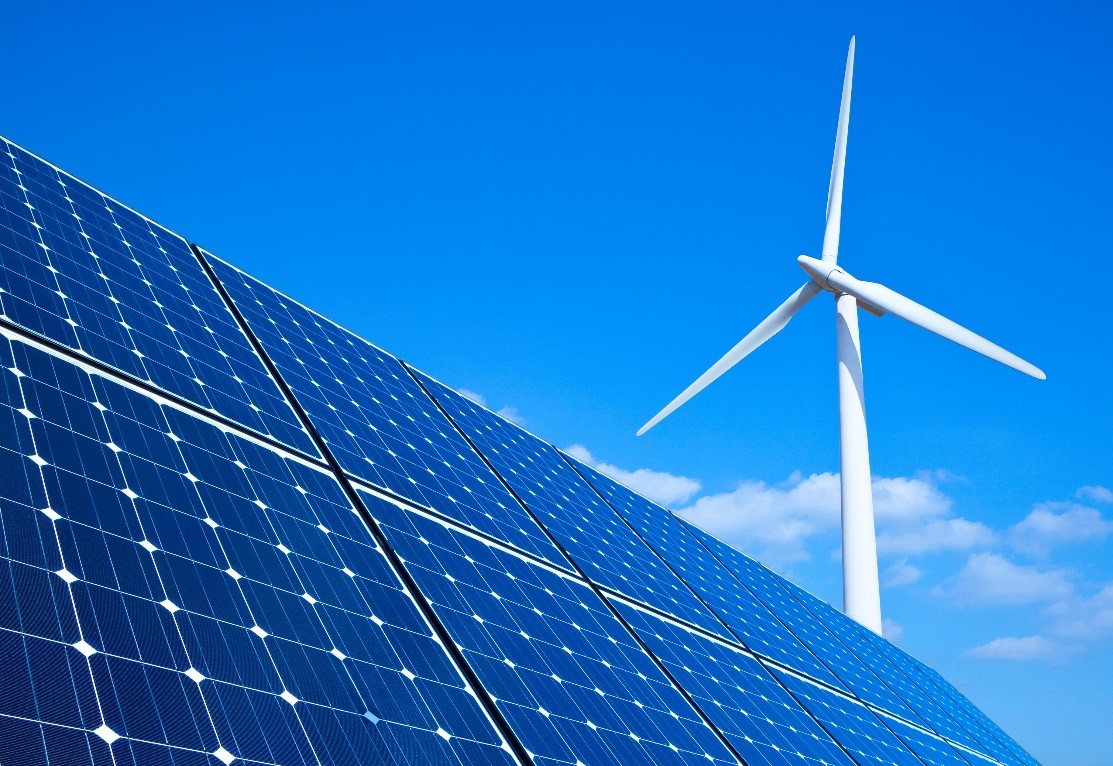 Solar panels extend upward toward a blue sky with a wind turbine in the background